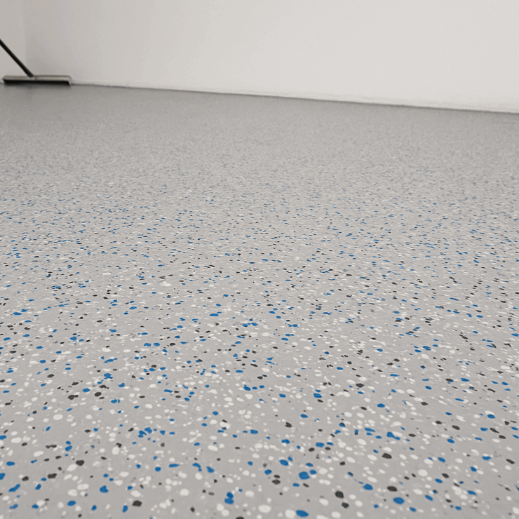 Epoxidharz-Chipsboden mit grauer Grundfläche und farbigen Flakes in Blau, Schwarz und Weiß in breitem Raumformat