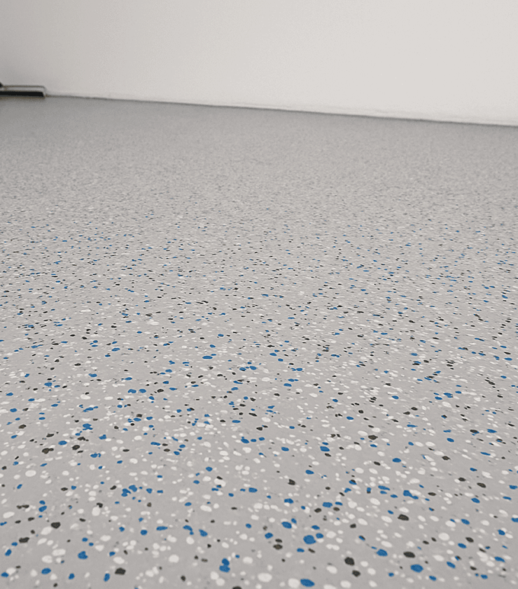Epoxidharz-Chipsboden mit grauer Grundfläche und farbigen Flakes in Blau, Schwarz und Weiß in breitem Raumformat